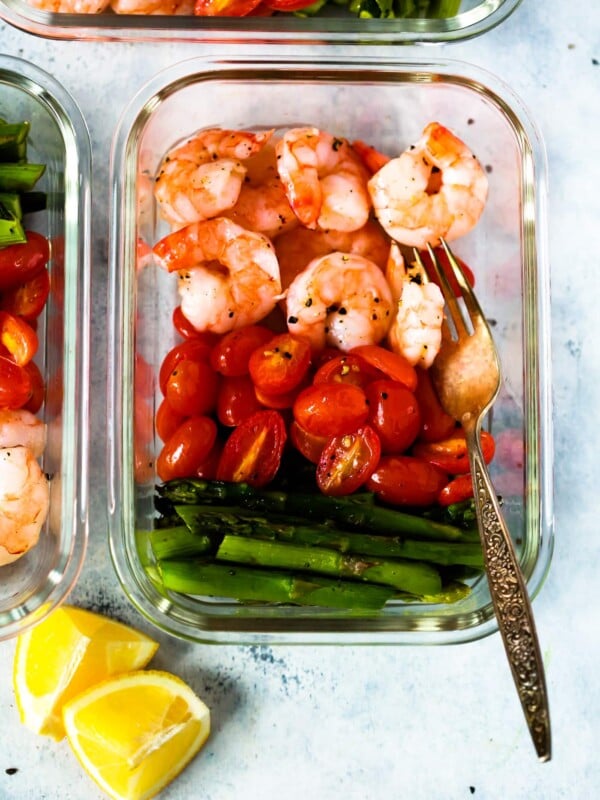 A glass meal prep container with shrimp, cherry tomatoes, and asparagus.