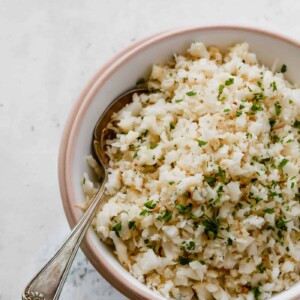Overhead photo of a bowl of garlic parmesan cauliflower rice with a spoon inside.