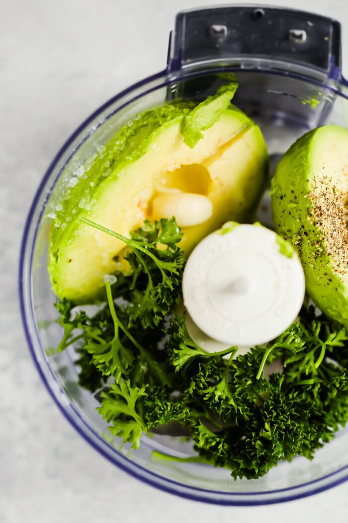 ingredients to make avocado sauce inside of a food processor.