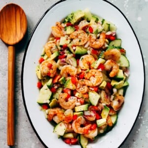 An oval serving platter container shrimp avocado cucumber salad.