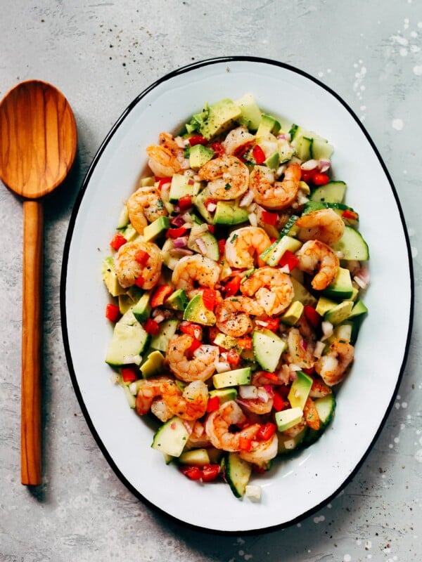 An oval serving platter container shrimp avocado cucumber salad.