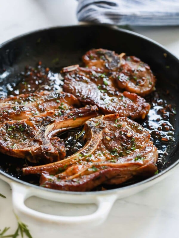 A close up of a white cast iron skillet containing Lamb Chops