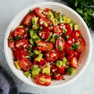 An overhead photo of an avocado tomato salad in a white bowl.