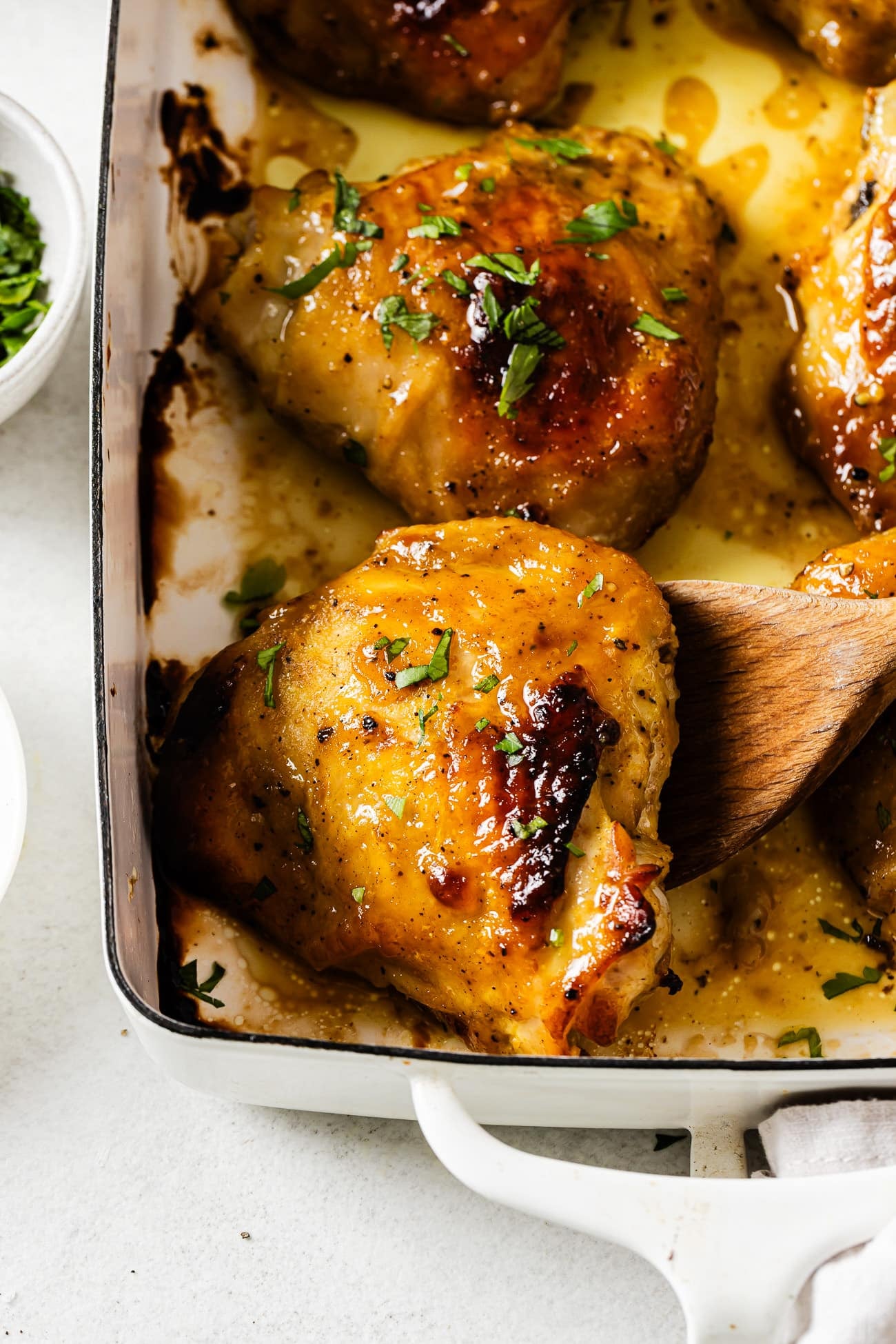 Closeup view of a baked chicken thighs on a white casserole.