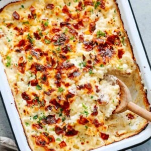 close up of a cauliflower casserole in a baking dish with a wooden spoon scooping.