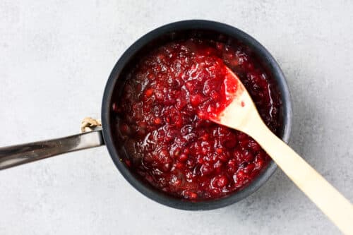 Cranberry sauce simmering in a pot with a wooden spoon.