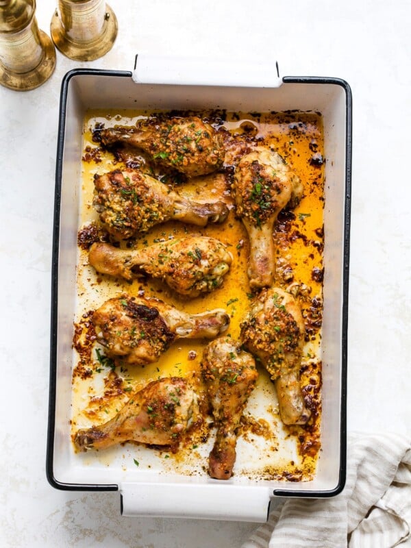 Garlic butter baked chicken drumsticks in a white baking dish.