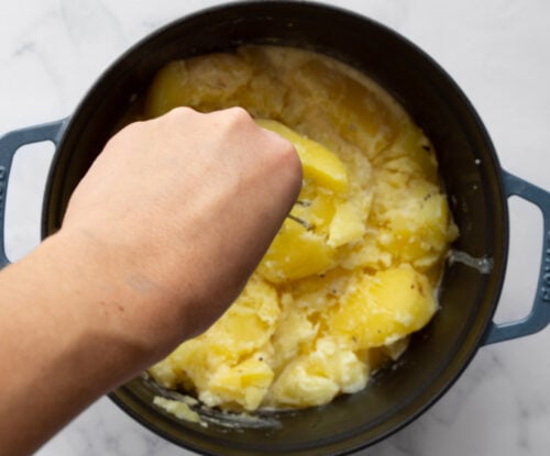 Hand mashing potatoes in a pot.