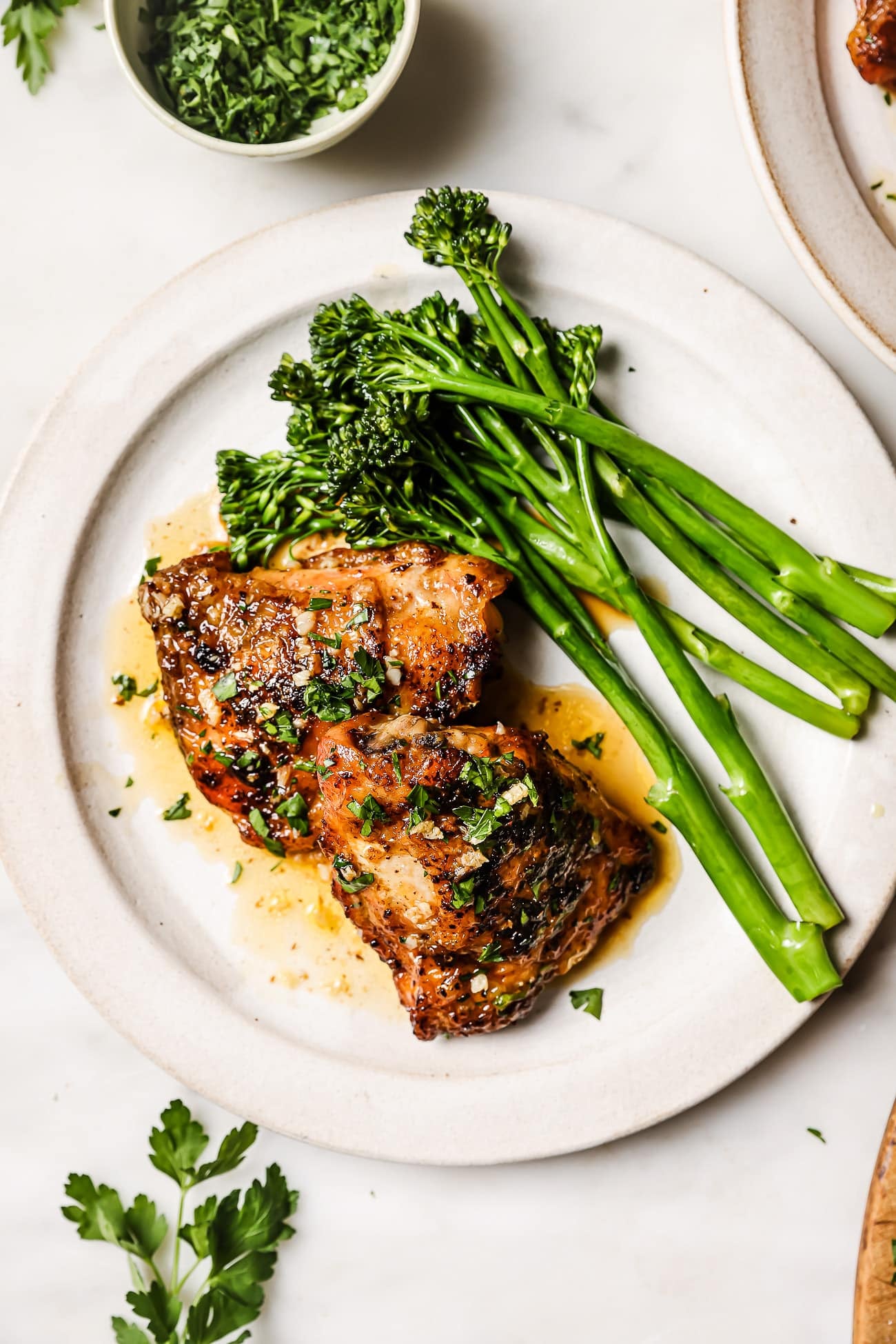 Chicken thighs on a white plate with green vegetables.
