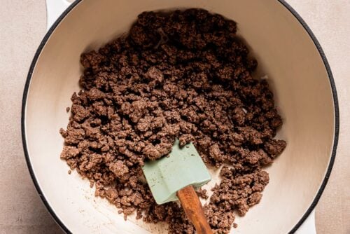 Cooked ground beef in a white pot being stirred with a green spatula, perfect as a savory base for Pasta e Fagioli Soup.