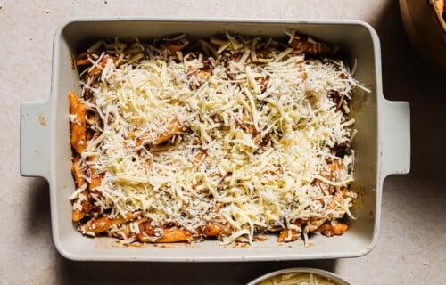 A rectangular baking dish filled with Baked Ziti with Ground Beef, covered in rich tomato sauce and generously topped with shredded cheese, ready to be baked.