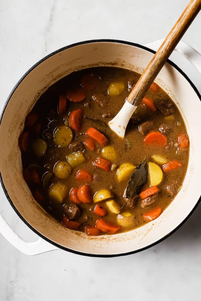 Apple cider beef stew in a large Dutch oven with a wooden spoon in it.