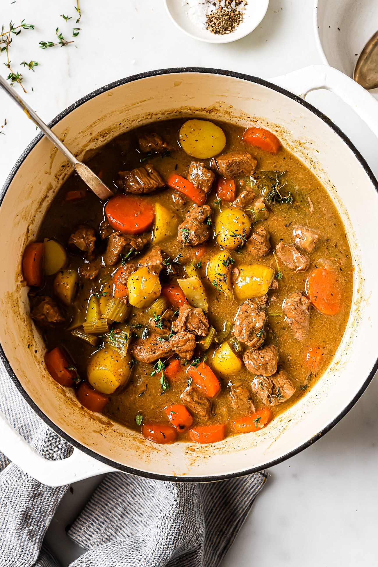 An overhead view of apple cider beef stew in a white Dutch oven.