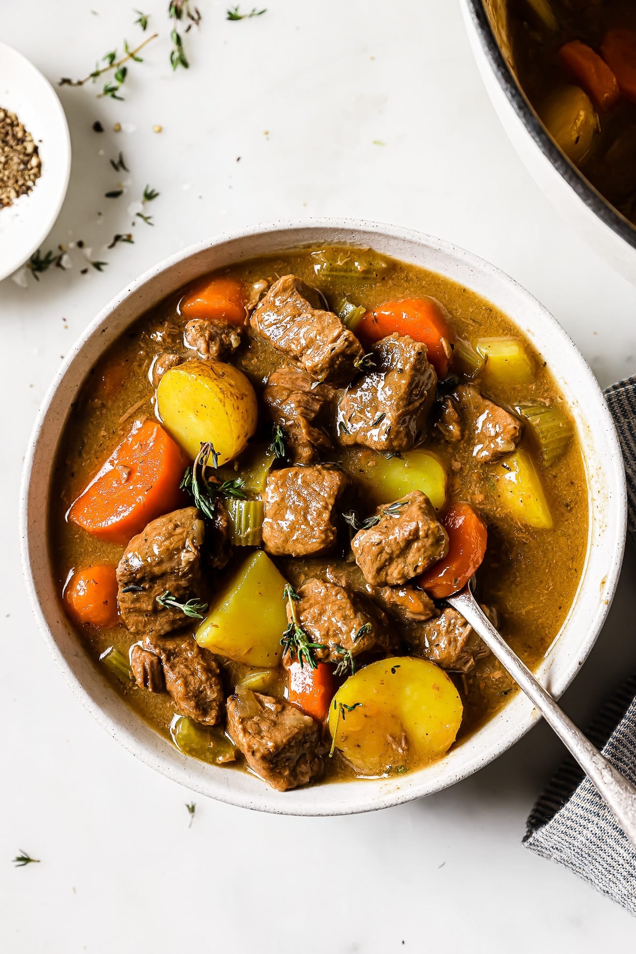 An overhead view of apple cider beef stew in a white bowl with a silver spoon in it. 