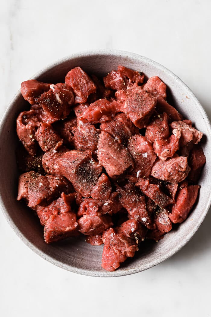 A bowl of beef stew meat seasoned with salt and black pepper in a bowl.
