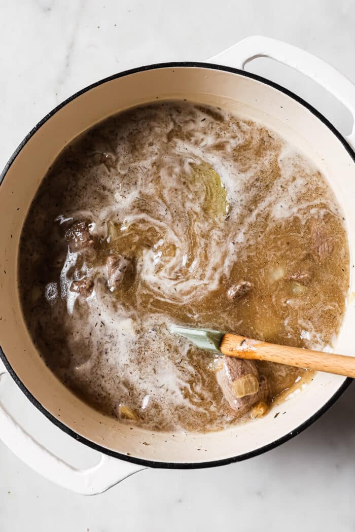 Beef stew in a Dutch oven with a wooden spoon in it.