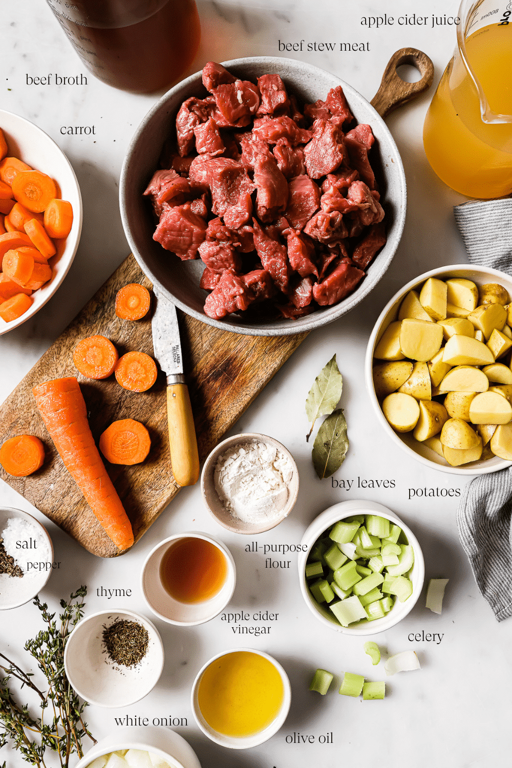 Apple cider beef stew ingredients in small bowls on a white countertop.