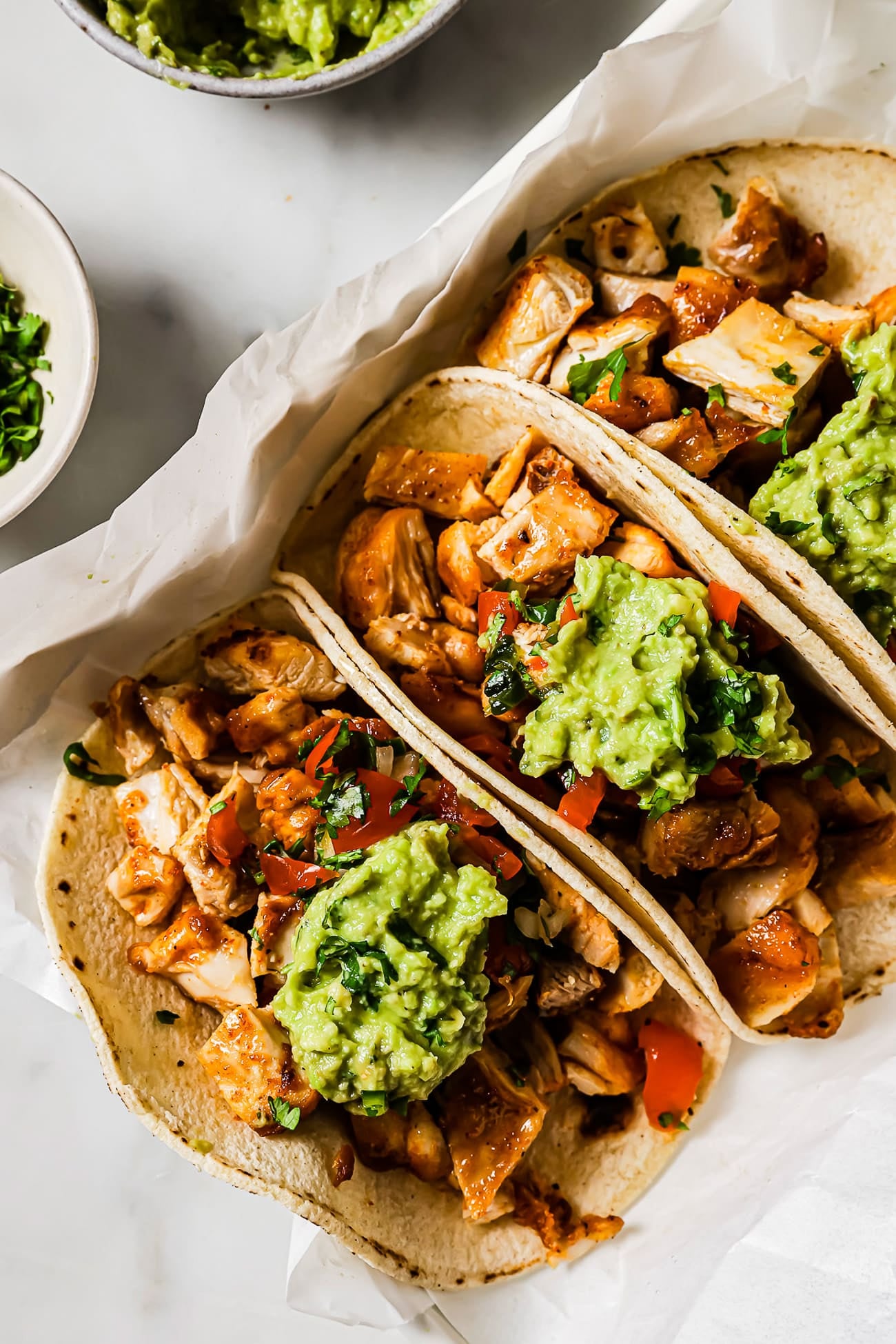 An overhead view of three chicken tacos topped with Pico de Gallo and guacamole.     