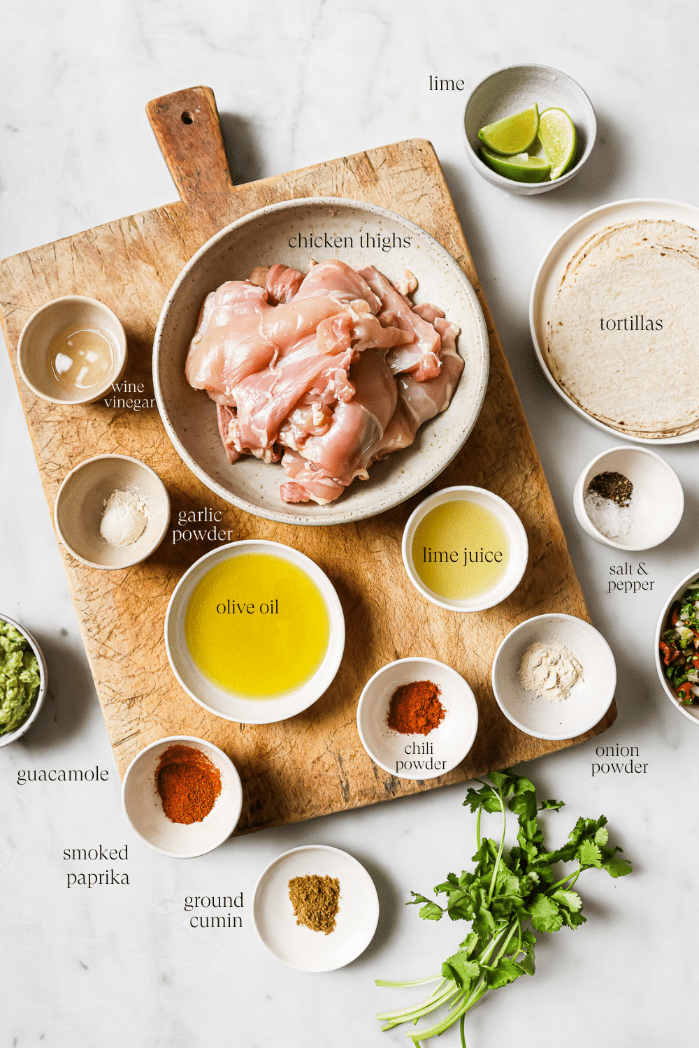 Bowls of prepped ingredients on a wooden cutting board and white countertop.