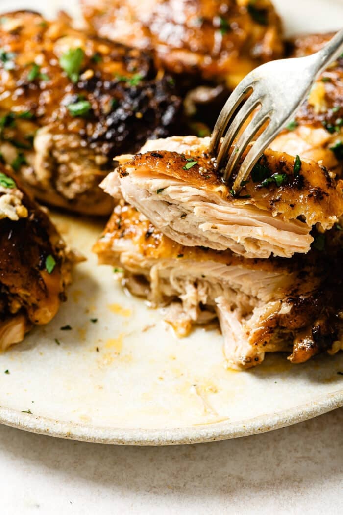 A fork picking up a slice of slow cooker chicken thighs.