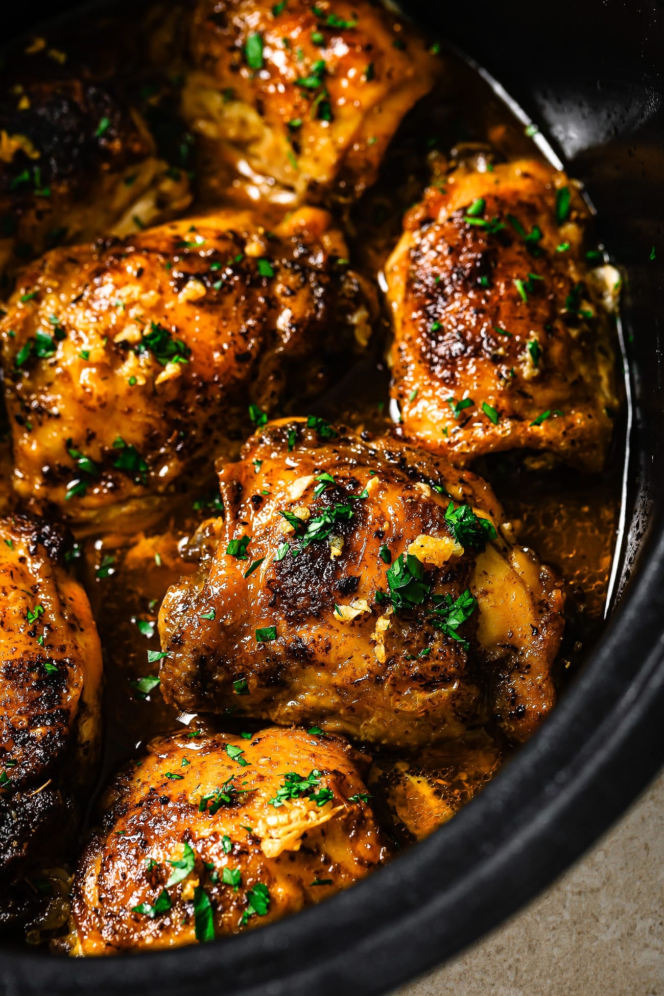A close-up of slow cooker chicken thighs garnished with parsley in a black slow cooker. 