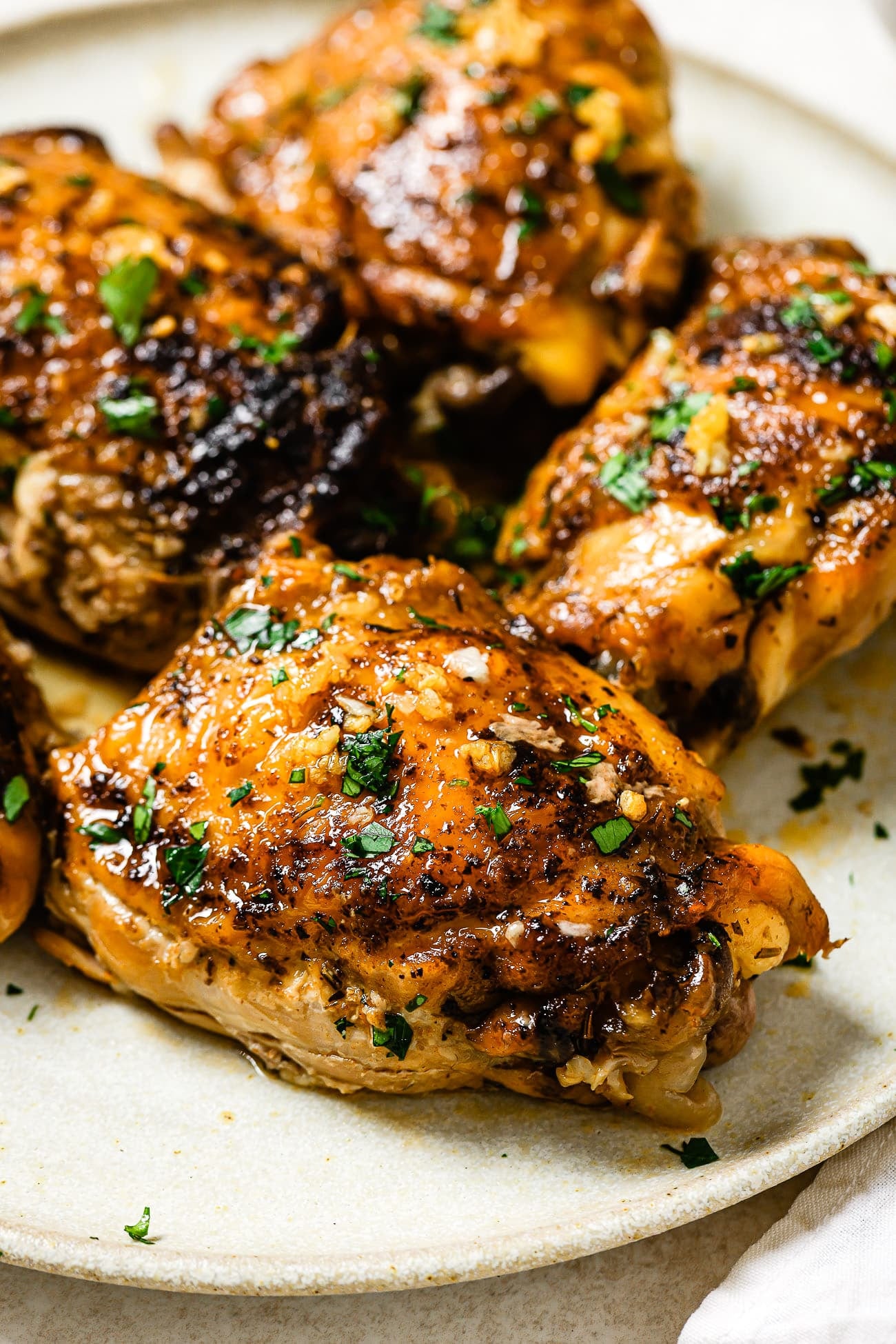 A closeup of slow-cooker chicken thighs garnished with parsley on a white serving plate.