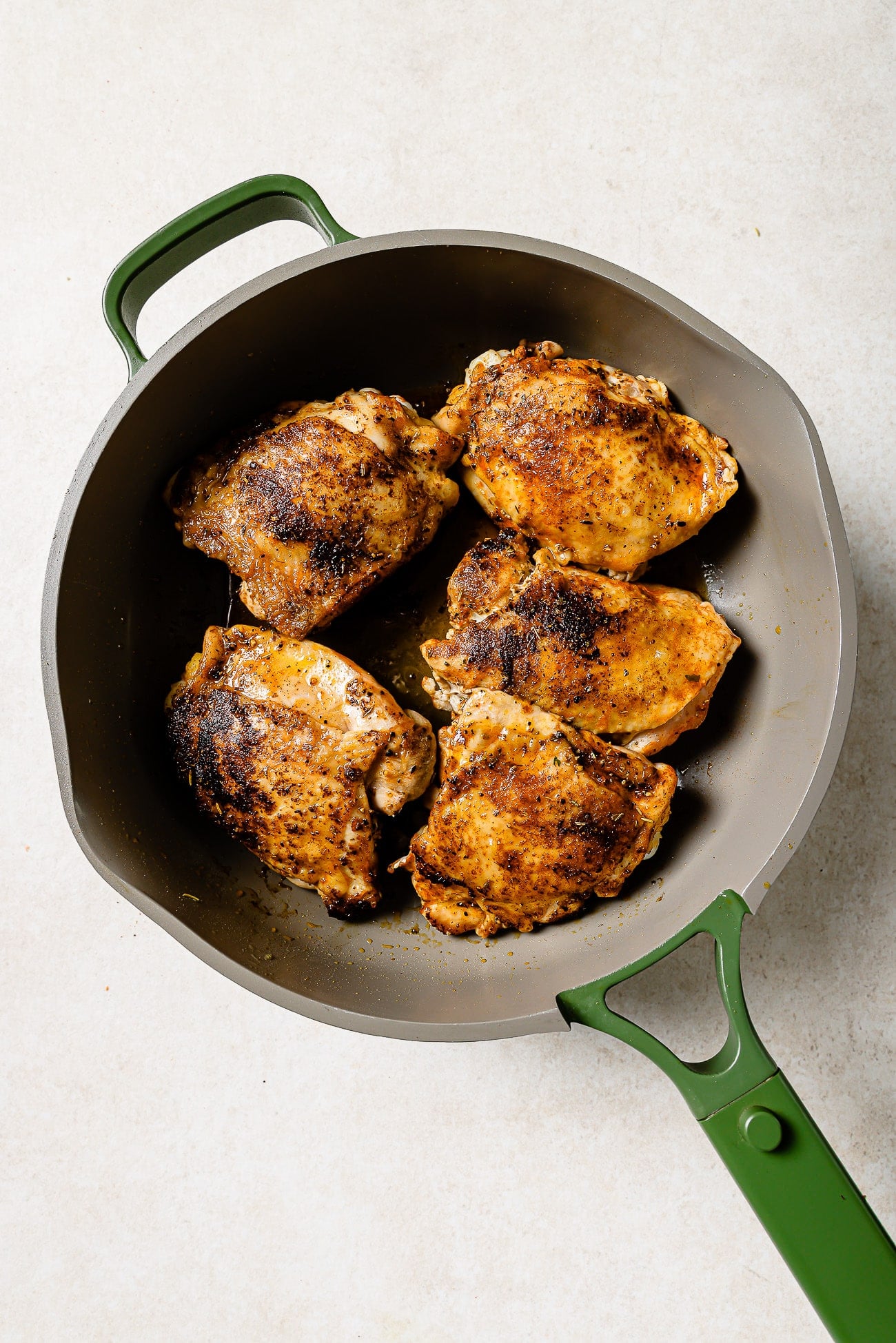 Five seared chicken thighs in a large cast iron skillet.