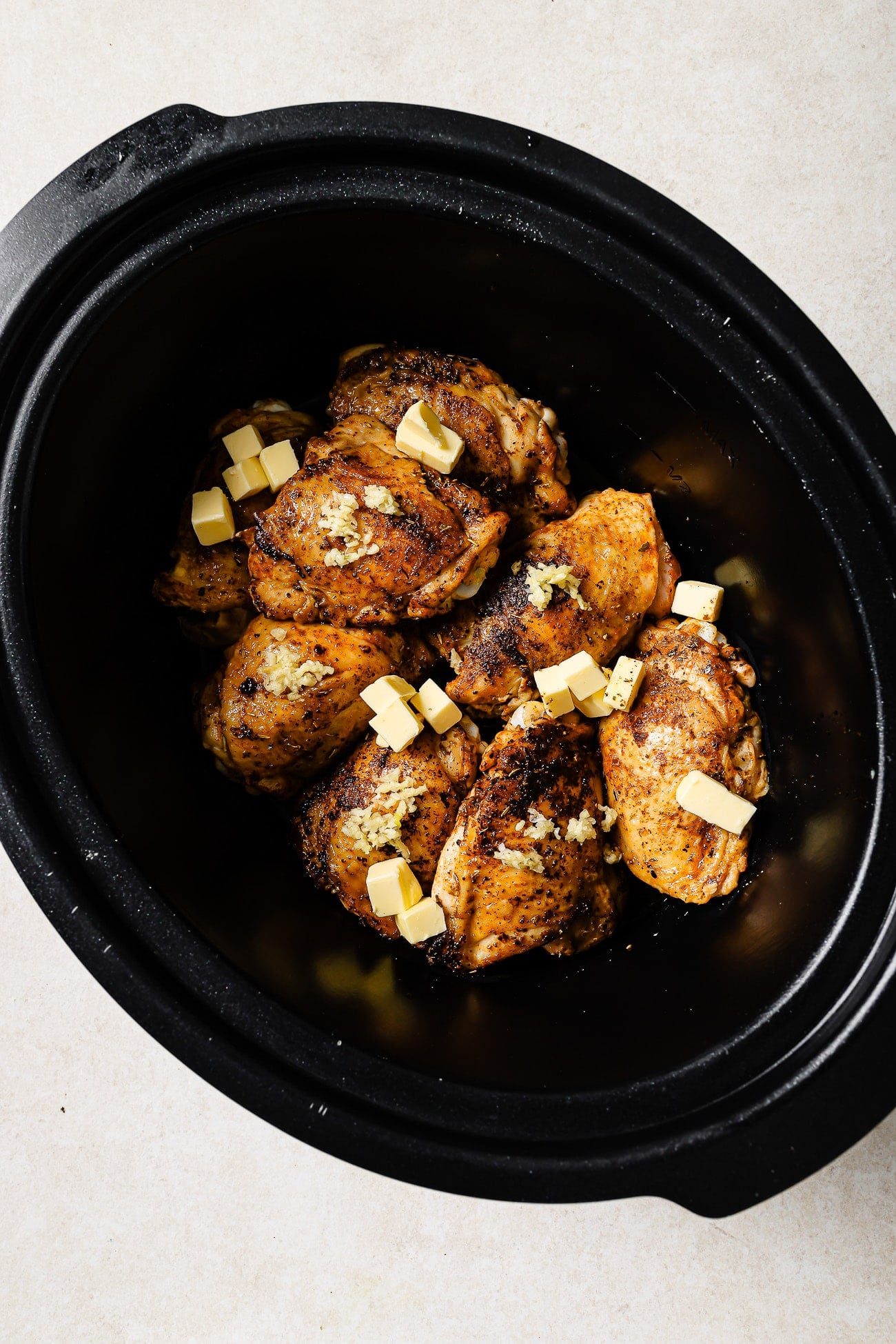 Seared chicken thighs in a slow cooker with butter and garlic on top.