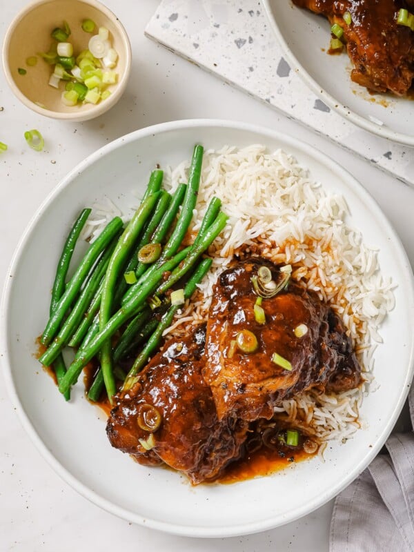 Slow Cooker chicken thighs on a white plate with green beans and rice.