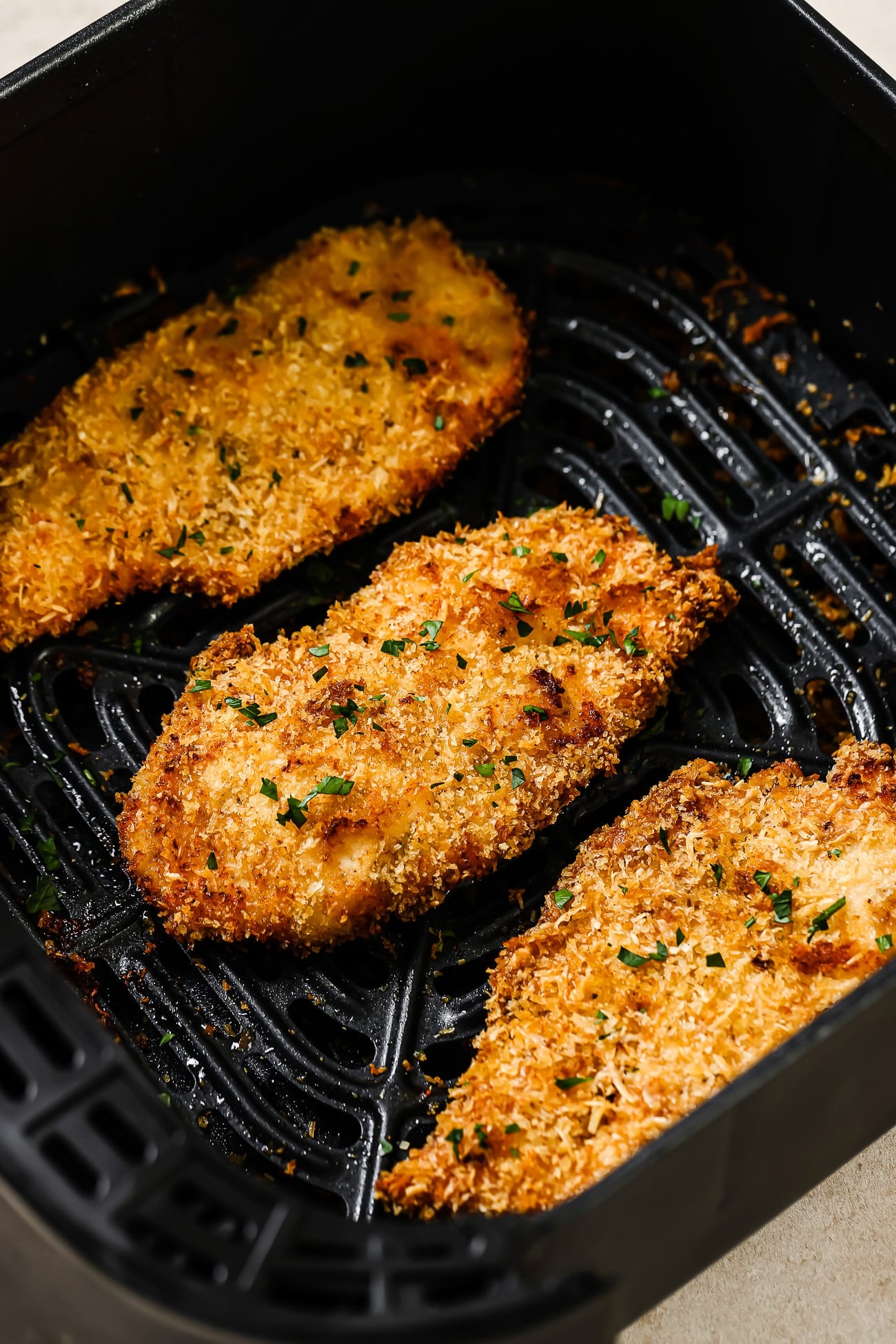 Three breaded chicken cutlets in an air fryer basket. 