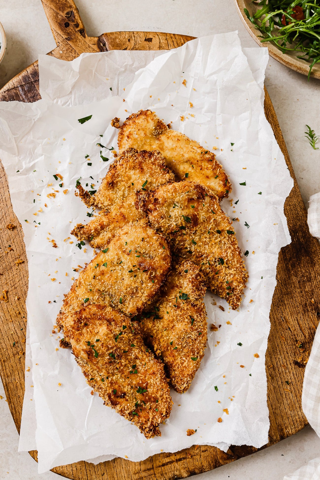An overhead view of air fryer chicken cutlets on parchment paper and a cutting board.