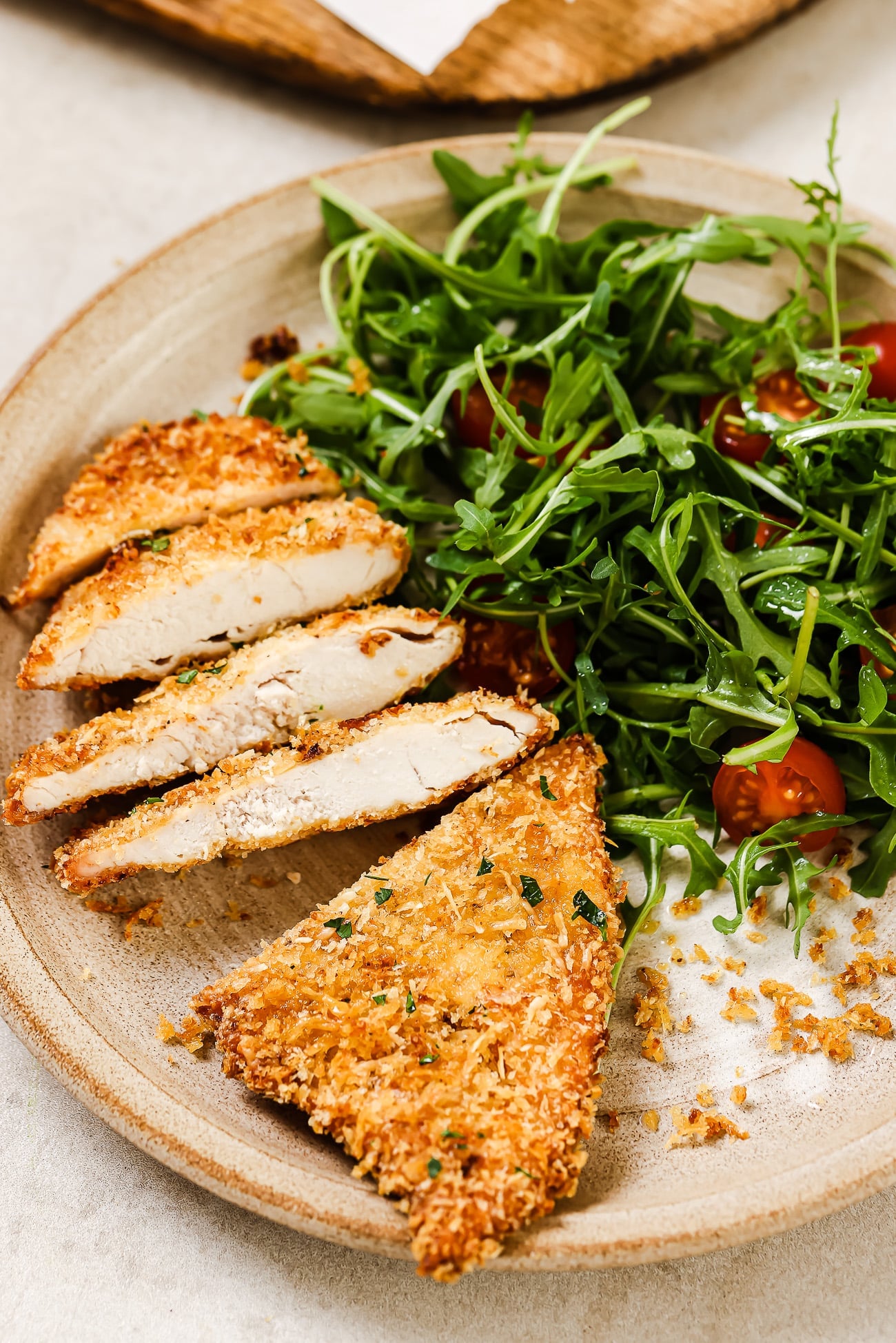 A sliced air fryer chicken cutlet on a plate with a side salad.