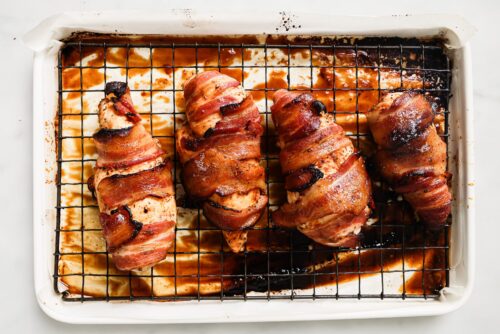 bacon wrapped chicken breast on top of a rack and a baking sheet