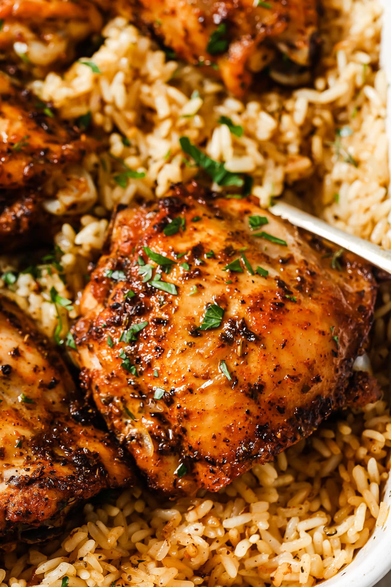 A closeup of baked chicken thighs over rice in a white baking dish.