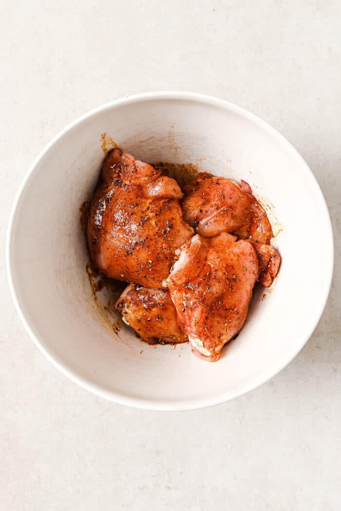 An overhead view of marinated chicken thighs in a white serving bowl.