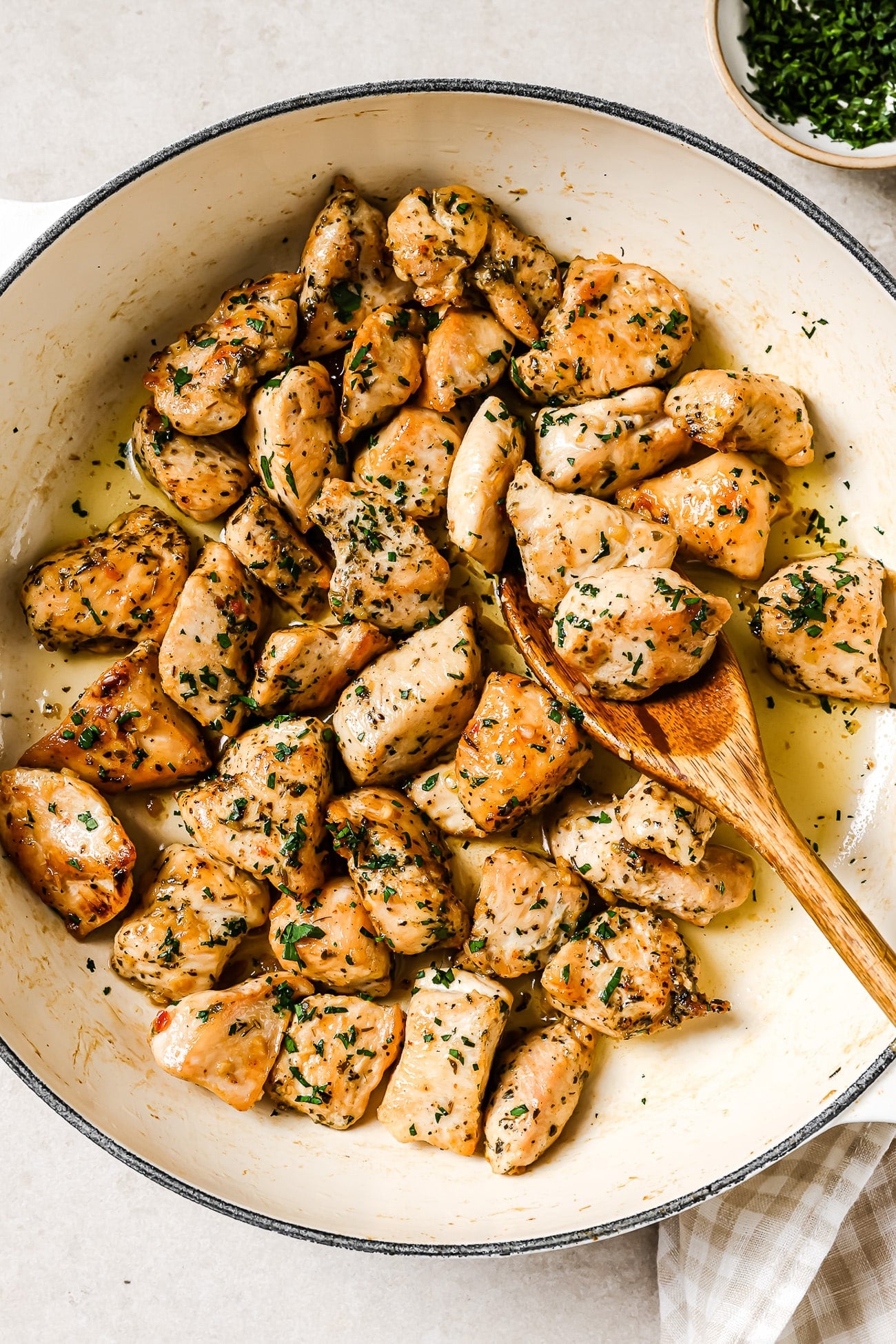An overhead view of garlic butter chicken bites in a skillet with a wooden spoon in it. 