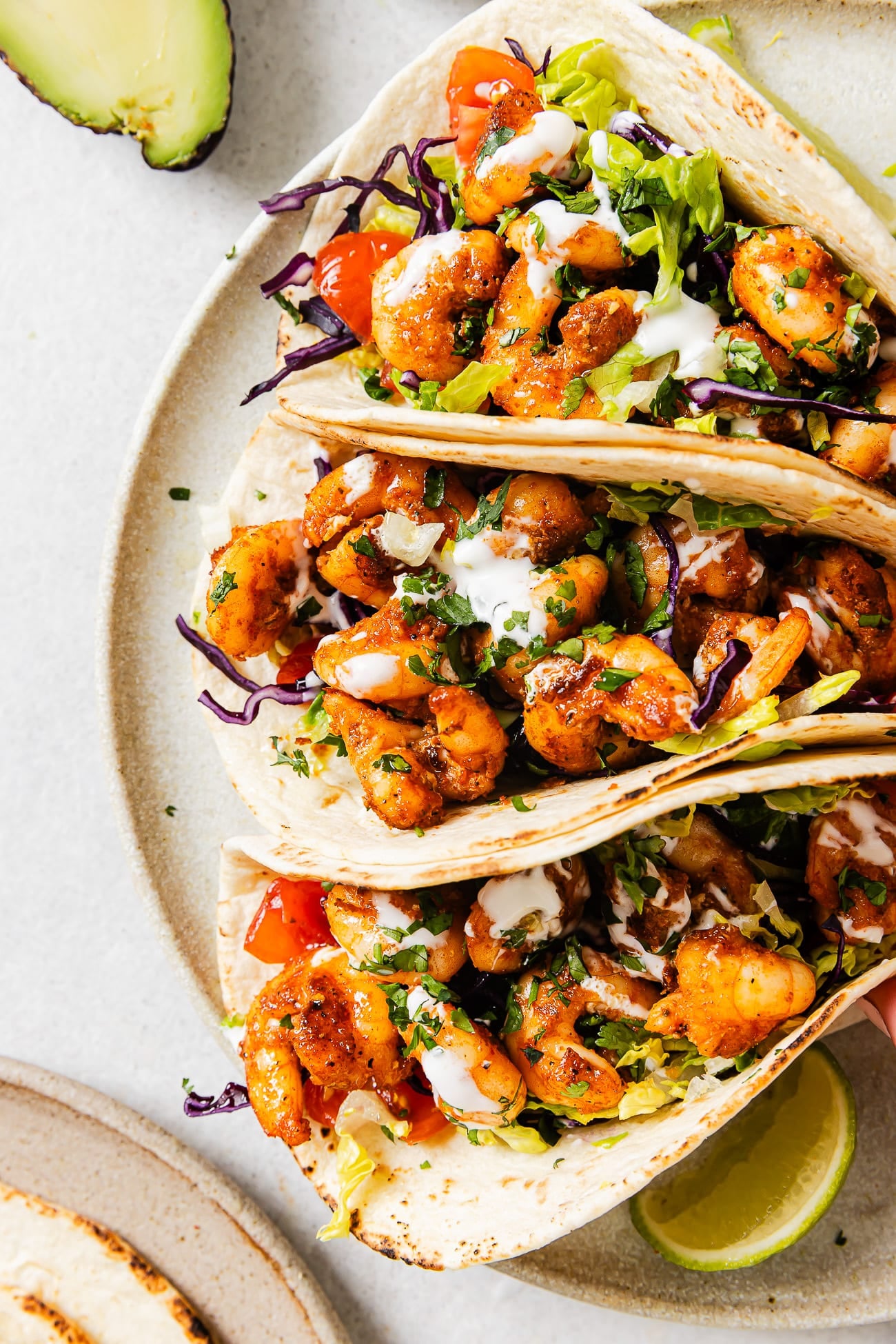 An overhead view of three shrimp tacos on a white serving plate. 