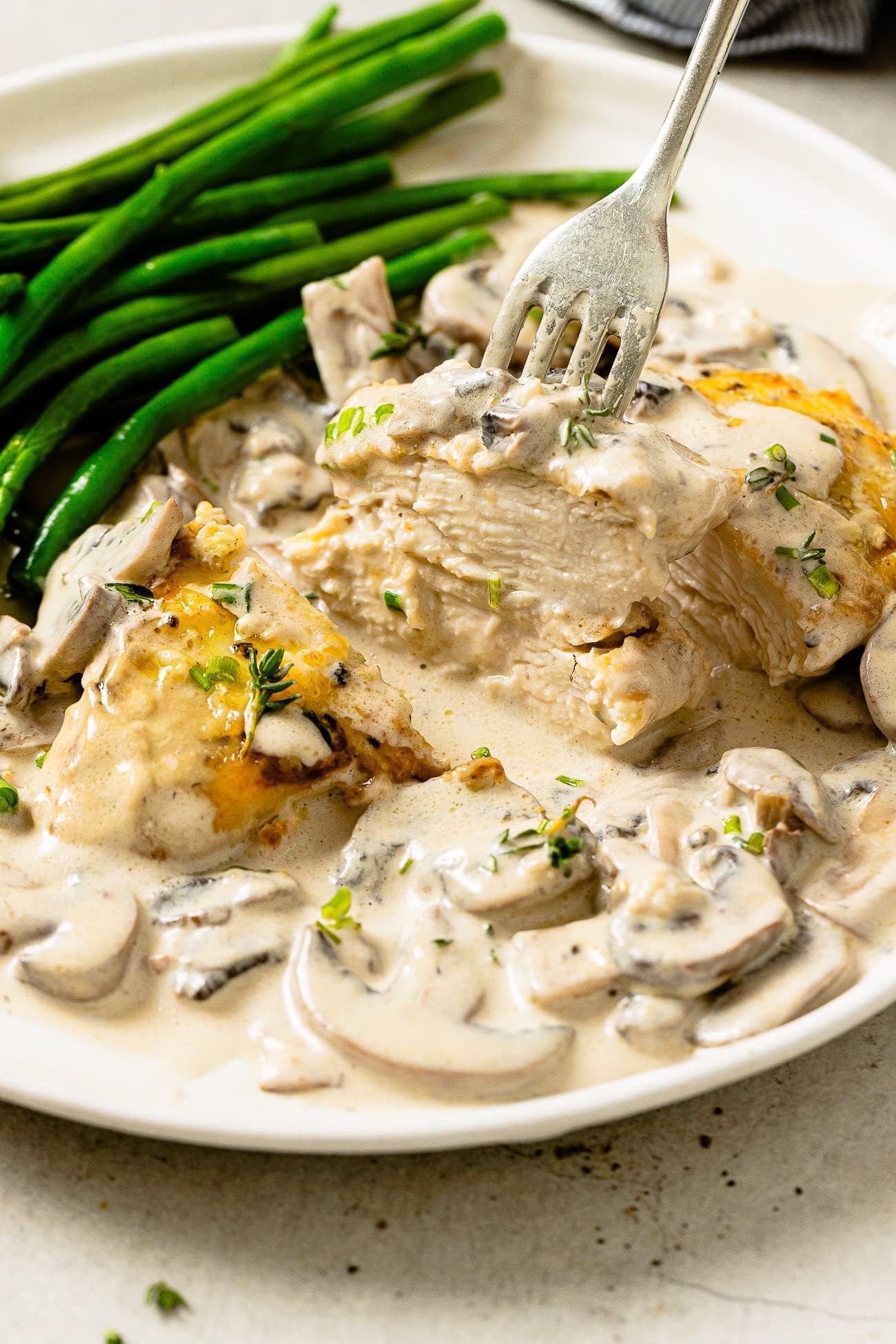 A serving of creamy mushroom chicken on a white plate with a side of green beans.