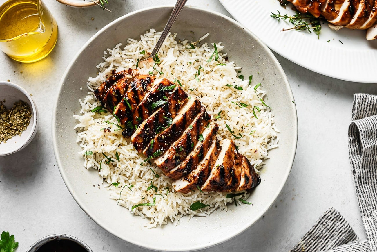 Balsamic chicken served over white rice on a white plate.