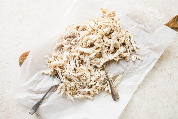 Juicy shredded chicken on a cutting board with two forks.