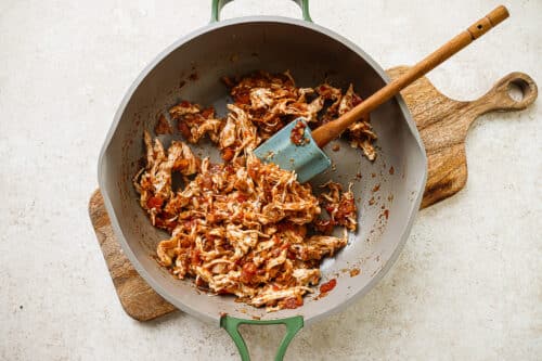 Tomato, onion, spice paste and chicken cooking in a skillet with spatula on a wooden board.