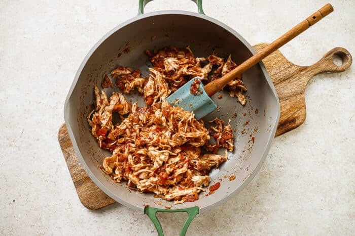 Tomato, onion, spice paste and chicken cooking in a skillet with spatula on a wooden board.
