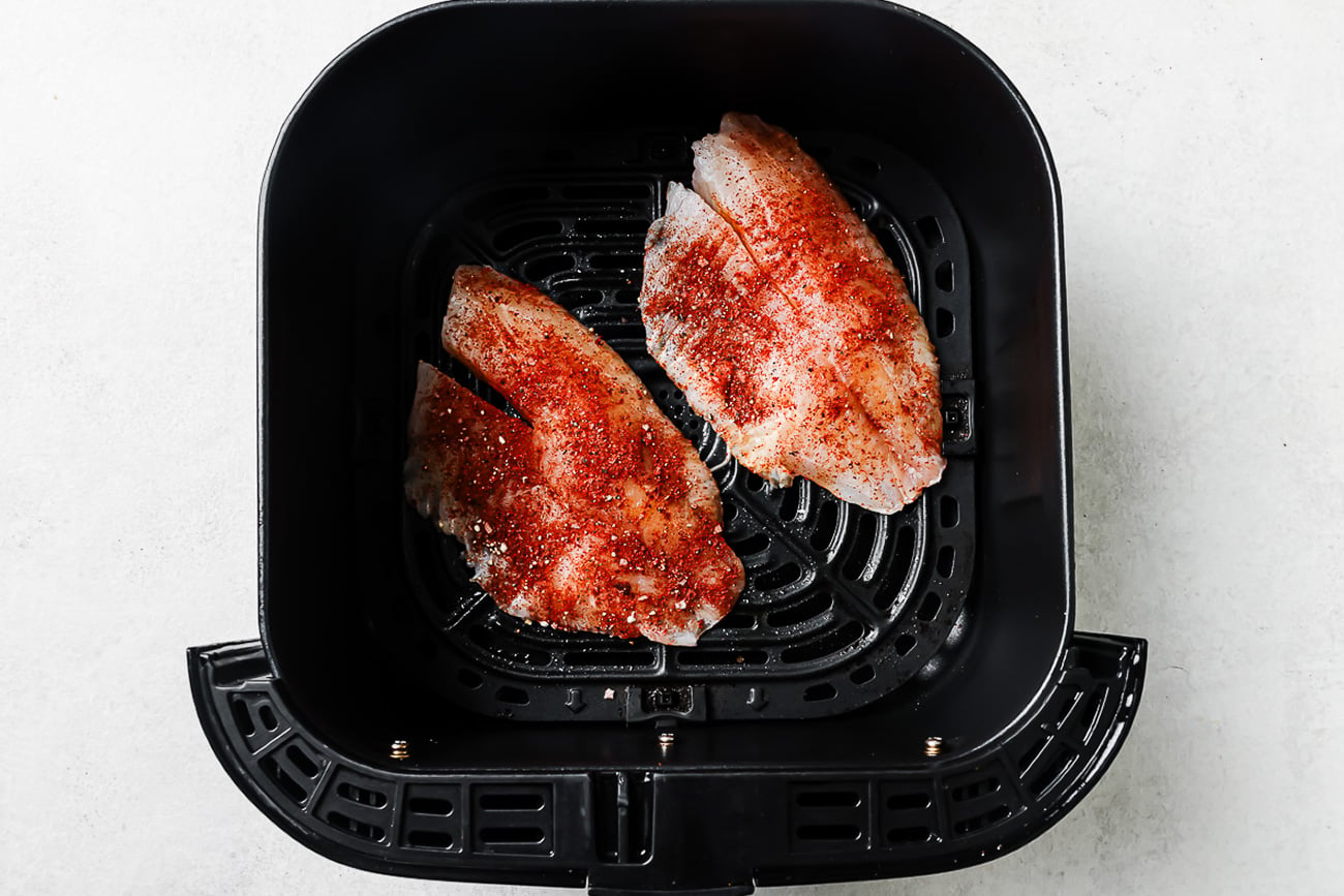 Seasoned raw tilapia in an air fryer basket.