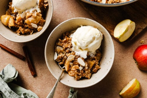 Gluten-free apple crisp in a white bowl topped with creamy vanilla ice cream for a cozy dessert.