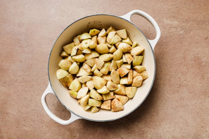 Diced and peeled apples mixed with warm spices in a white skillet, ready for baking.
