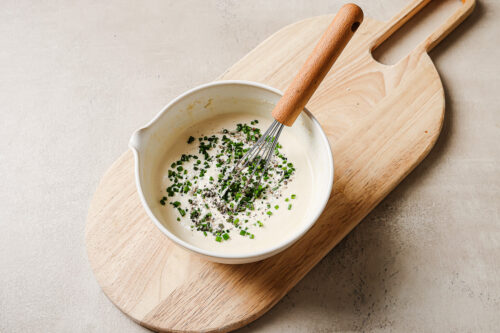 horseradish sauce in a white bowl with chives on a wooden board.