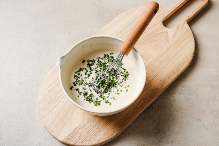 horseradish sauce in a white bowl with chives on a wooden board.