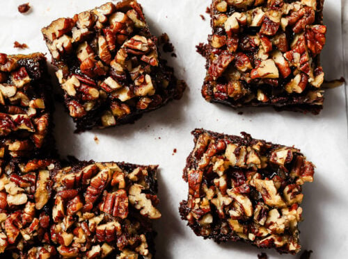Overhead view of pecan pie brownies cut into squares on parchment paper, featuring a gooey chocolate base and caramelized pecan topping.