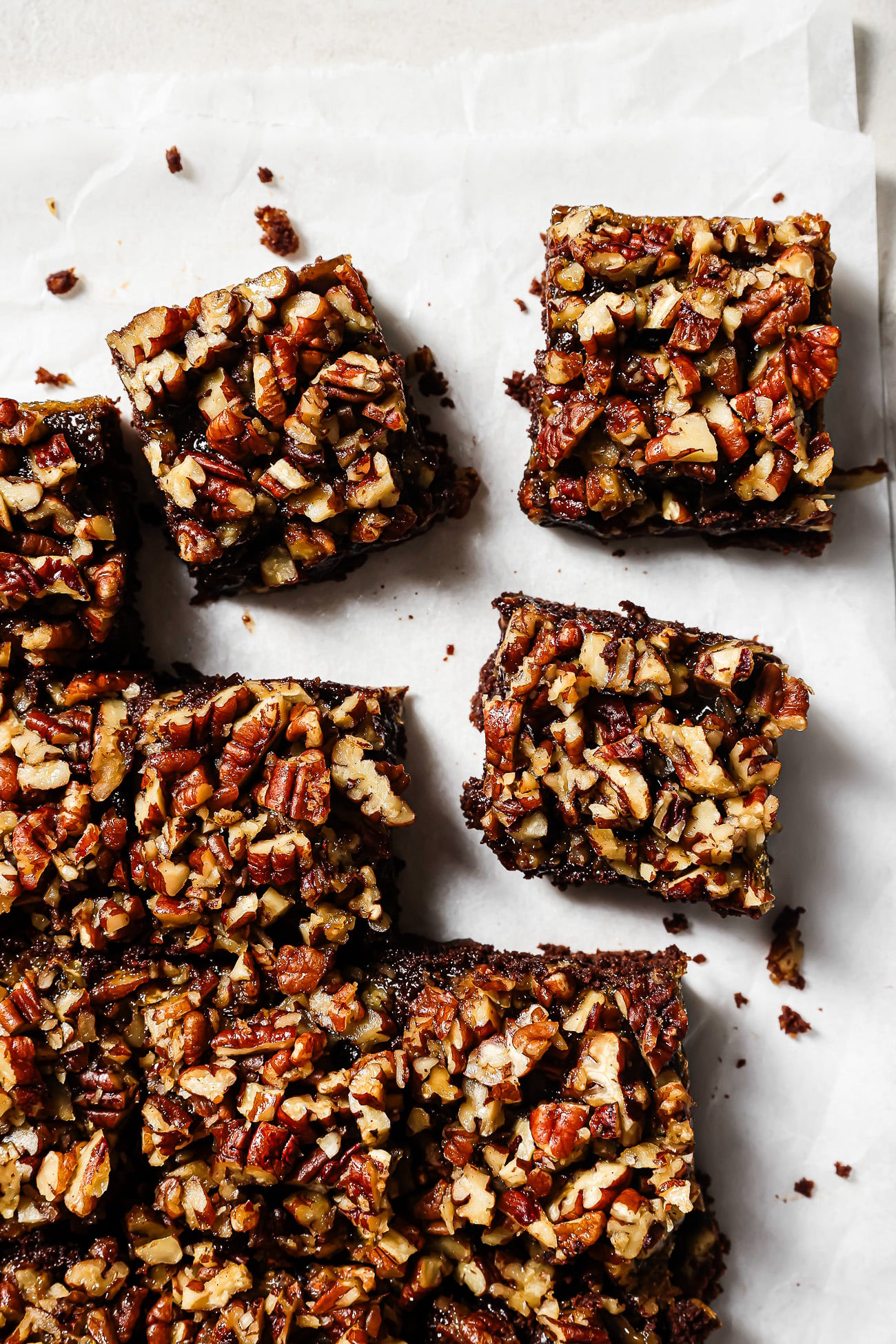 Overhead view of pecan pie brownies cut into squares on parchment paper, featuring a gooey chocolate base and caramelized pecan topping.