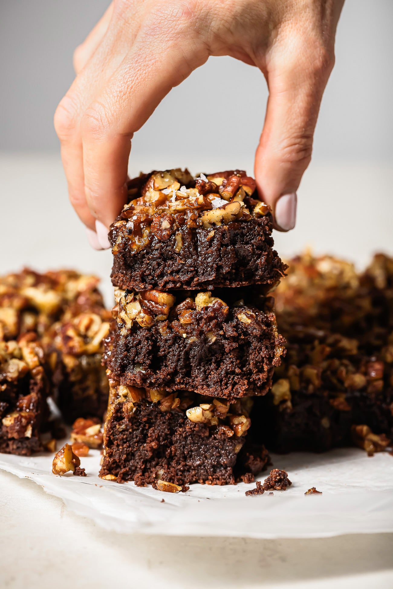 Hand holding a stack of gooey pecan pie brownies with a rich chocolate base and caramelized pecan topping.